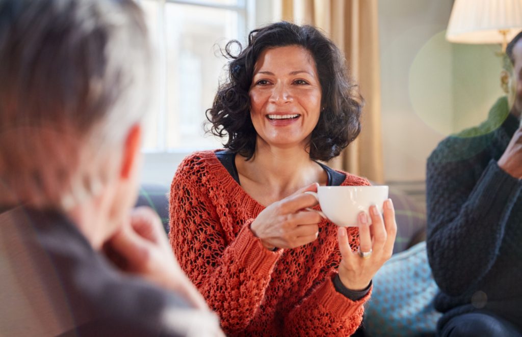 A woman talking to a man while drinking tea.