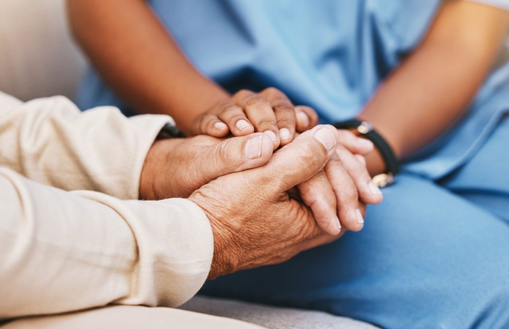 An elderly person holding hands with a nurse.